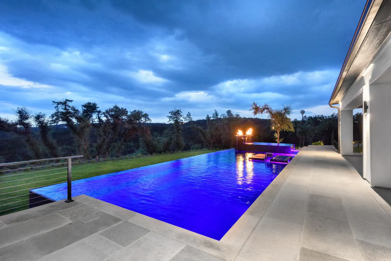 Long infinity-edge pool lit blue at dusk, the terrace in shadow — Estate Infinity, West Lake Hills