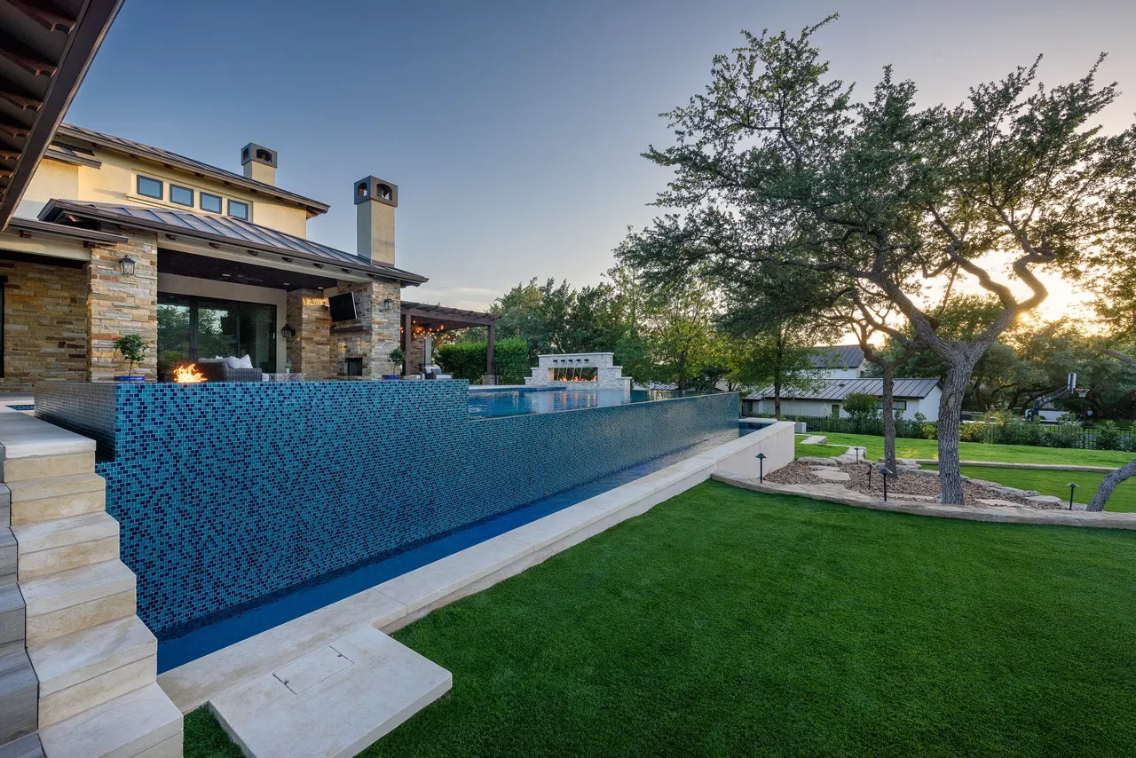 Infinity-edge estate pool with fire bowls at dusk by GB IV Designs