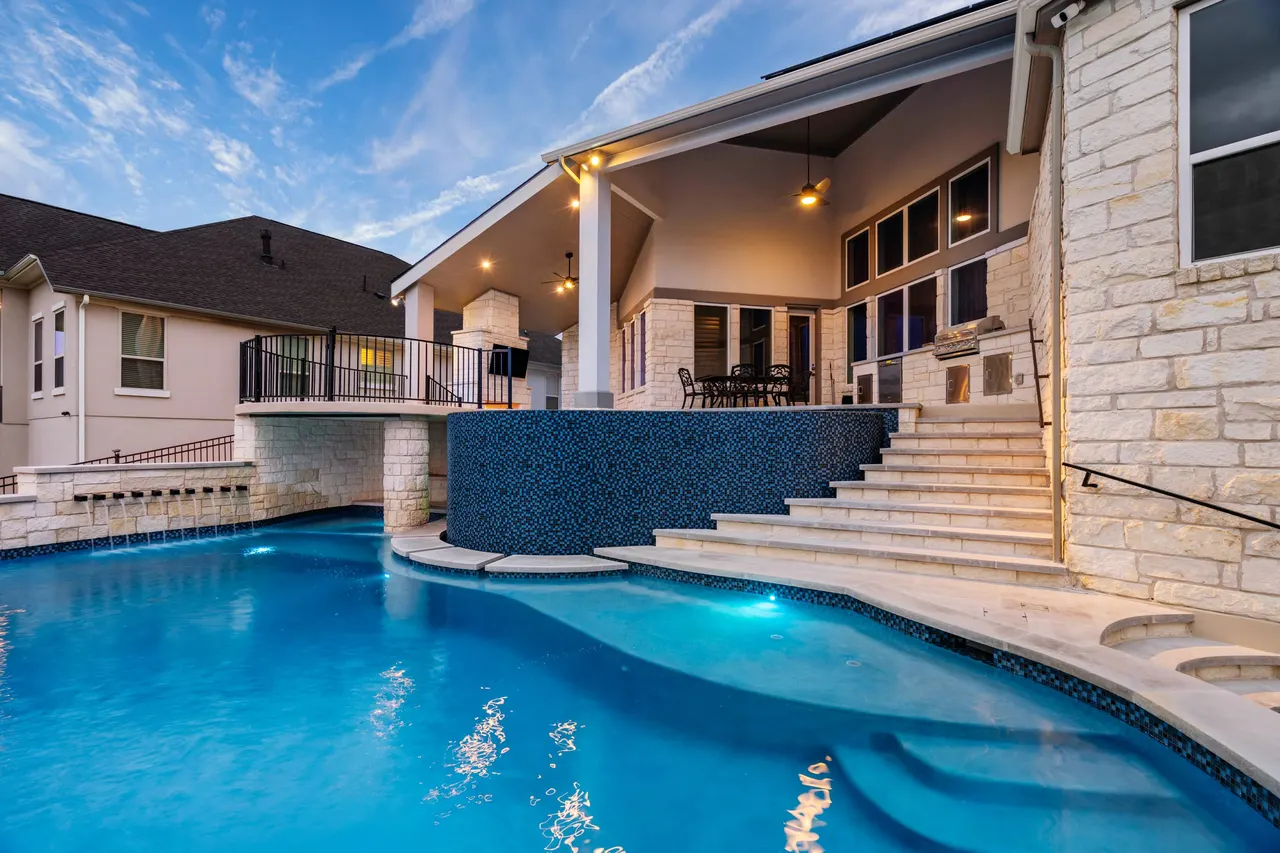 Freeform vanishing-edge pool and raised glass-tile spa by GB IV Designs, Bee Cave TX